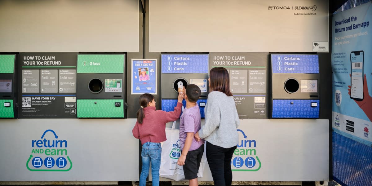 Person depositing bottles and cans into automated recycling return machine in New South Wales Australia