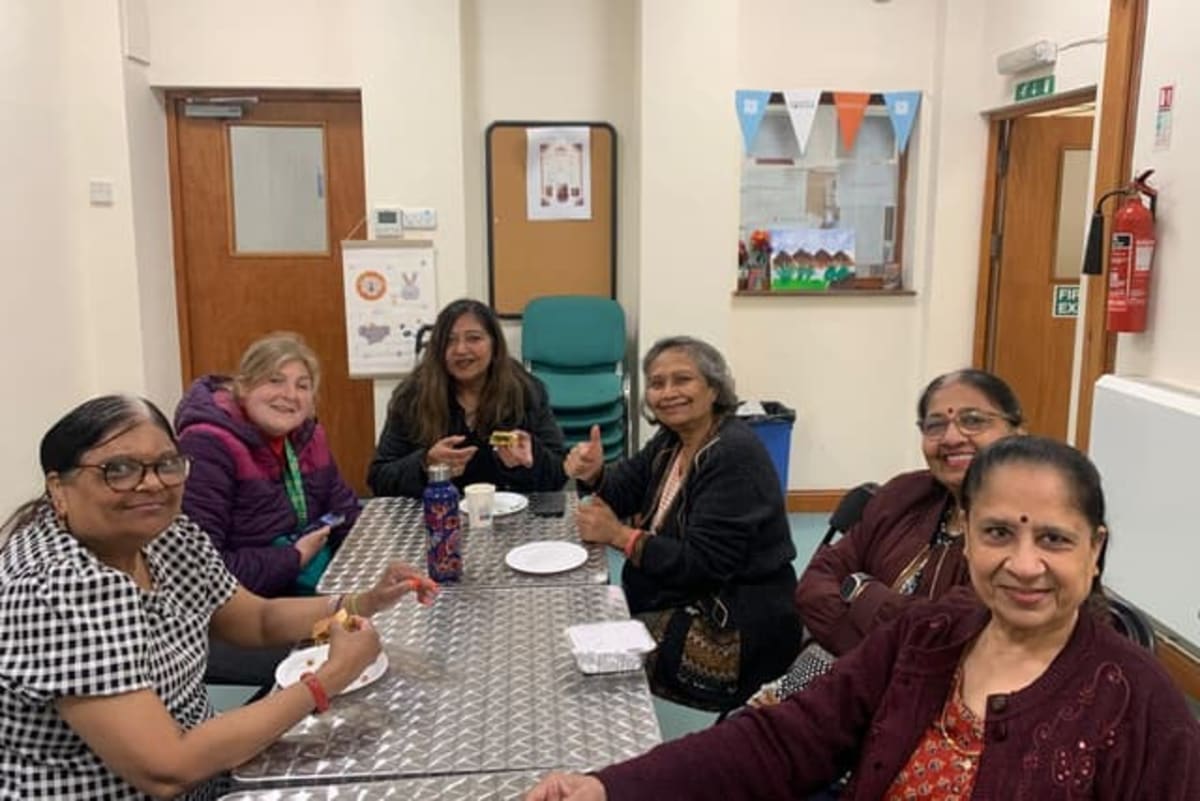 Women of diverse backgrounds gathering together at community café table sharing tea and conversation