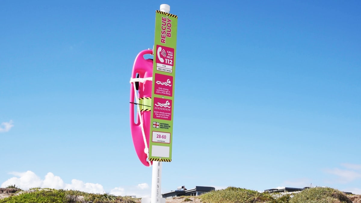 Bright pink rescue buoy mounted on pole at beach with ocean waves in background