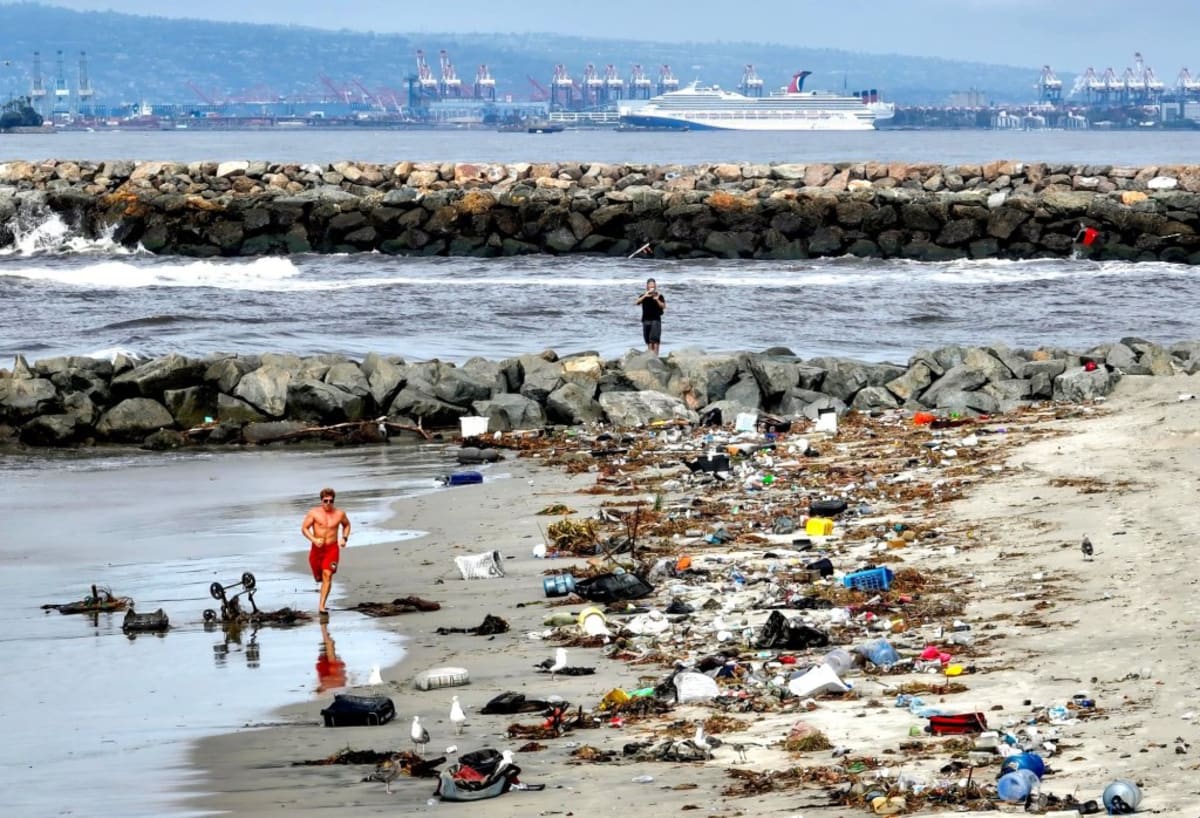 Trash and debris piled along San Gabriel River bank near Pacific Ocean in Seal Beach