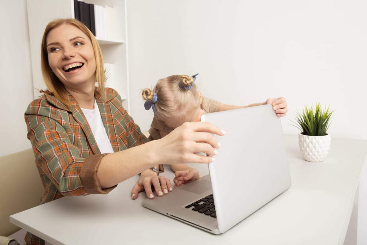 Parent working on laptop at home while baby plays nearby on floor
