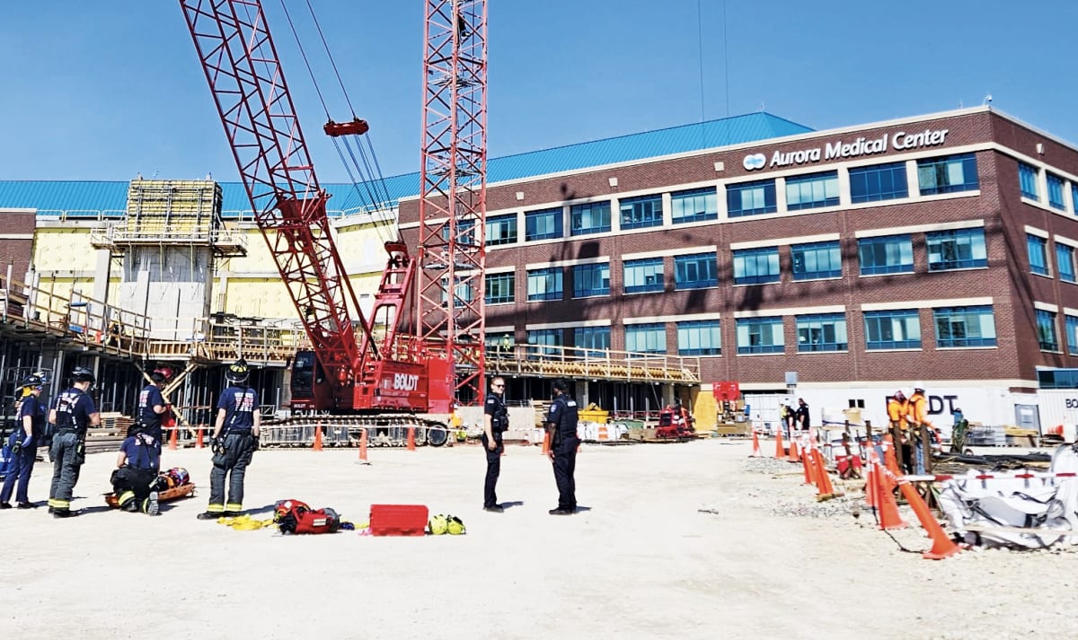 Firefighters performing high-angle rescue at top of construction crane next to hospital building