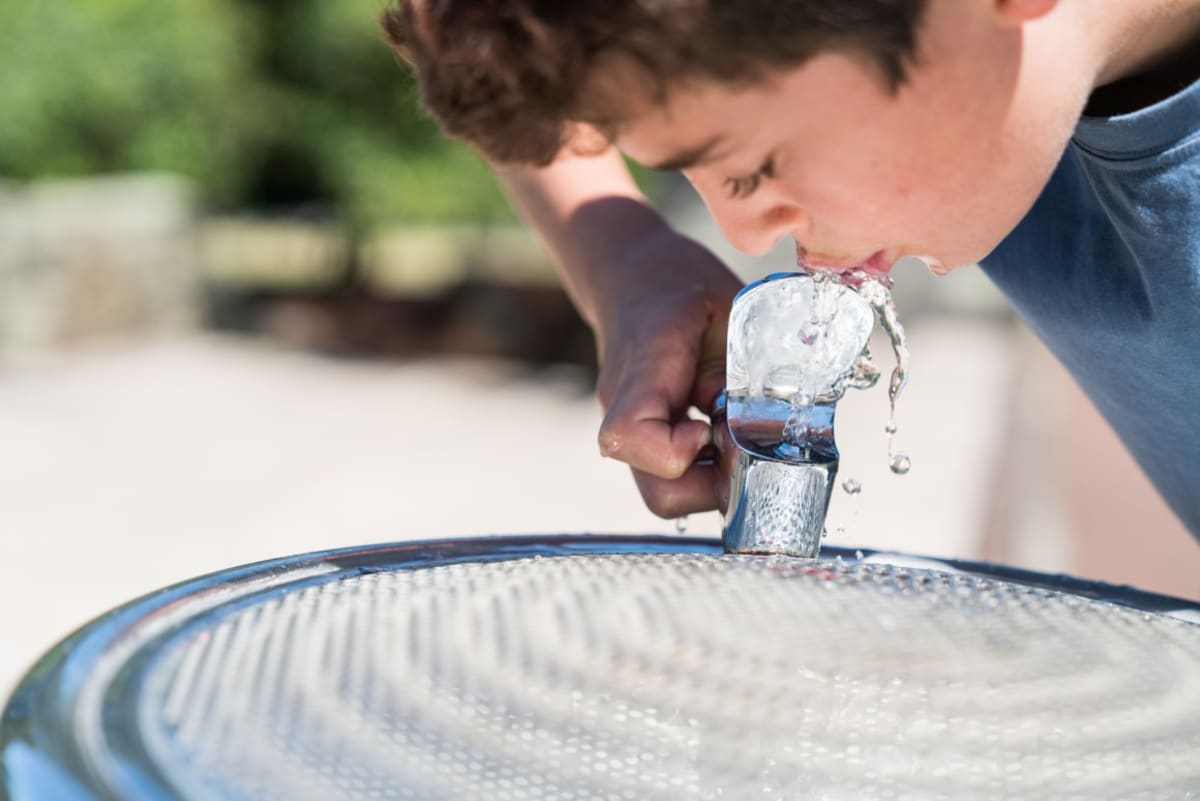 Modern public drinking fountain with multiple height spouts in sunny park playground