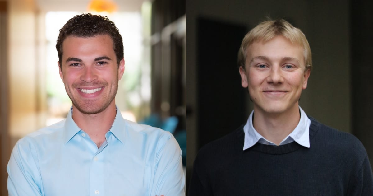 Two young male college students standing together in a chemistry laboratory smiling at camera