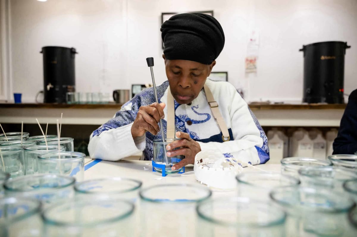 Refugee candlemaker pouring sustainable soy wax into recycled glass jar at Olympia workshop