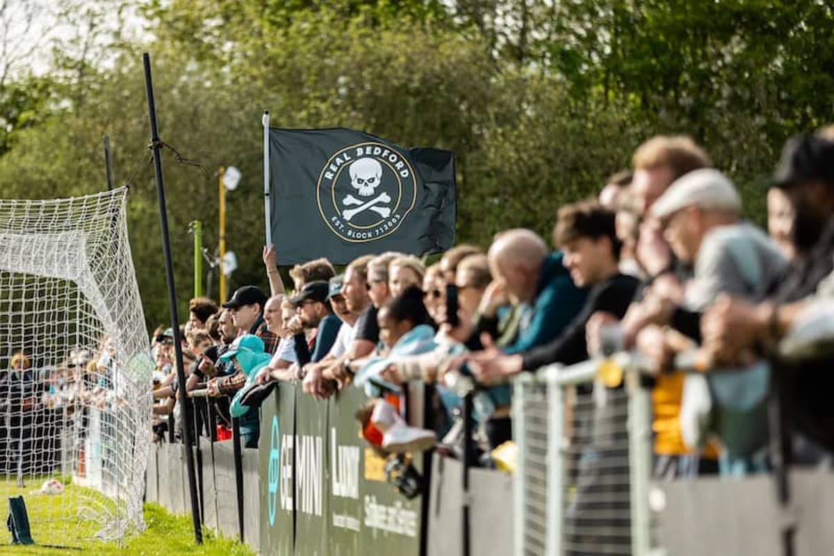 Packed crowd of football supporters standing pitch-side at small community stadium in England