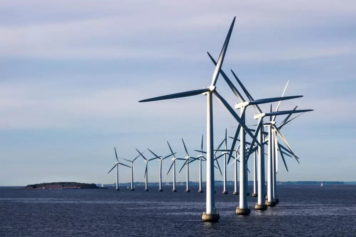 Solar panels and wind turbines along sunny Mediterranean coastline with blue sky