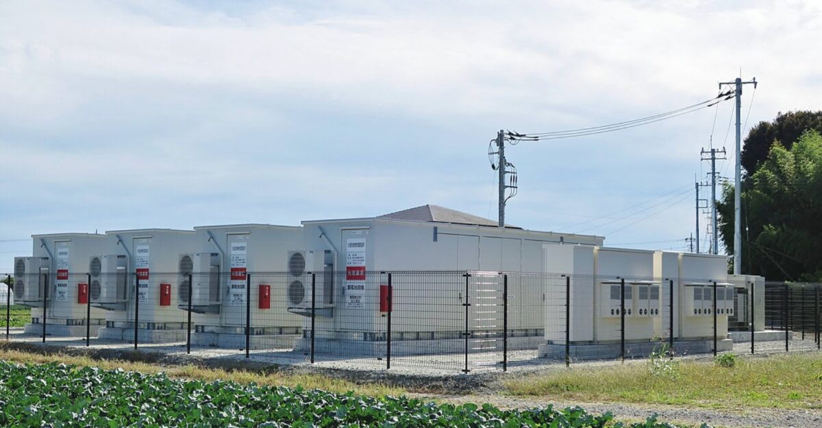 Large battery storage facility with rows of white containers next to solar panels under blue sky