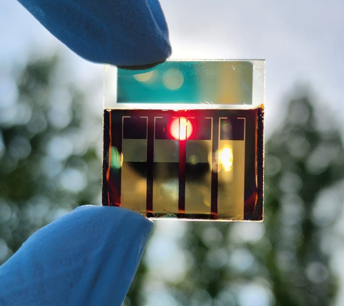 Closeup of ultra-thin flexible solar cell held between researcher's fingers in laboratory setting