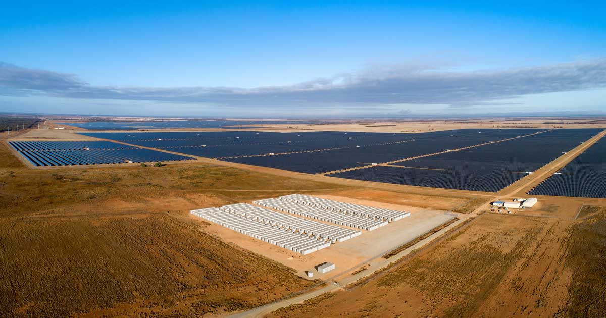 Large white Tesla Megapack battery units installed next to solar panel arrays in rural Australia