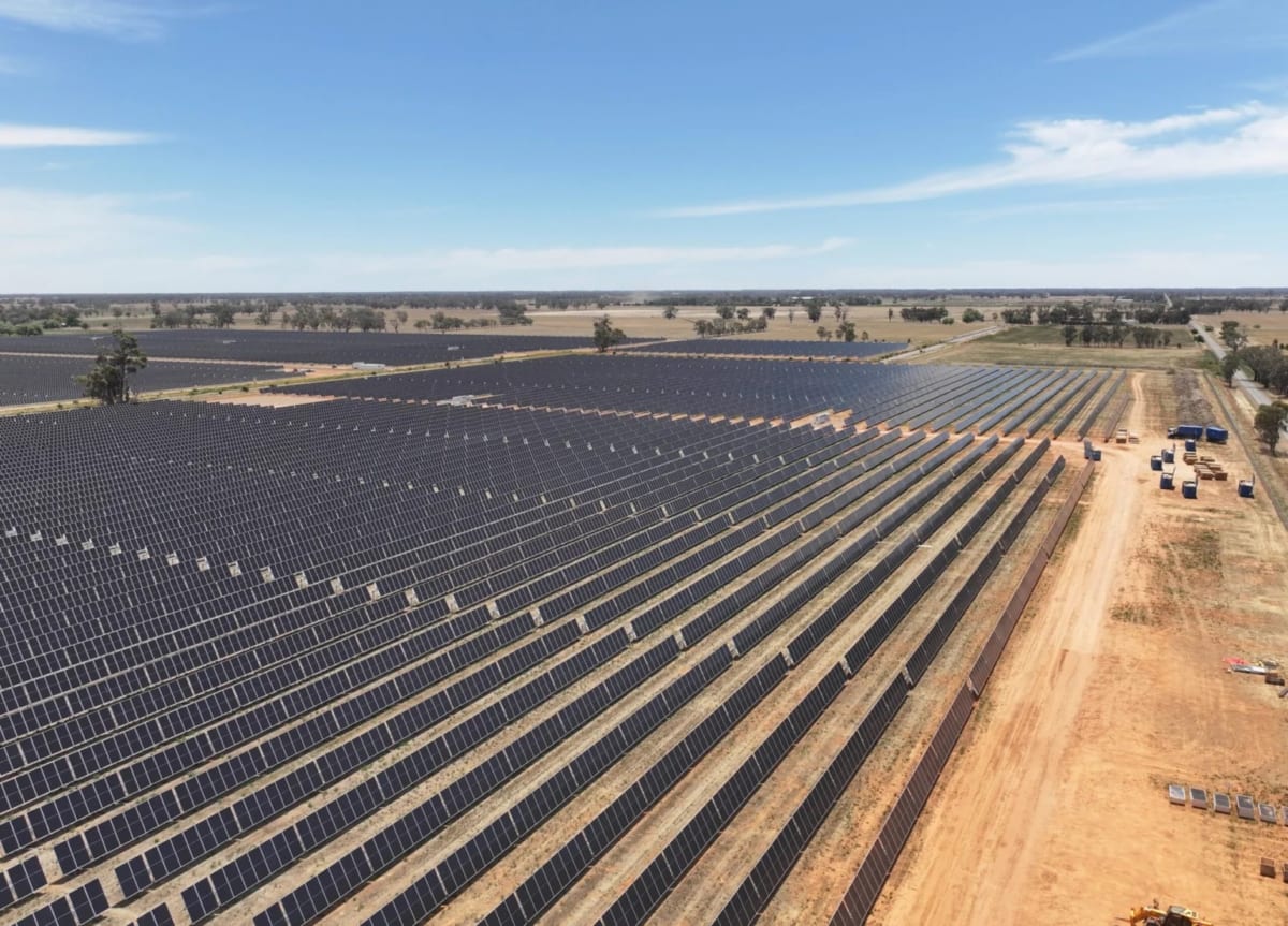 Large solar panel arrays stretching across Australian landscape under bright blue sky with battery storage facility
