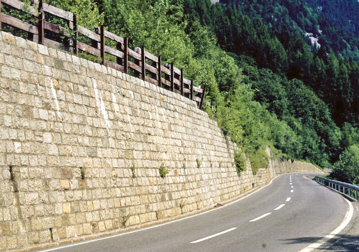 Solar panels mounted on concrete retaining wall alongside mountain road in Switzerland