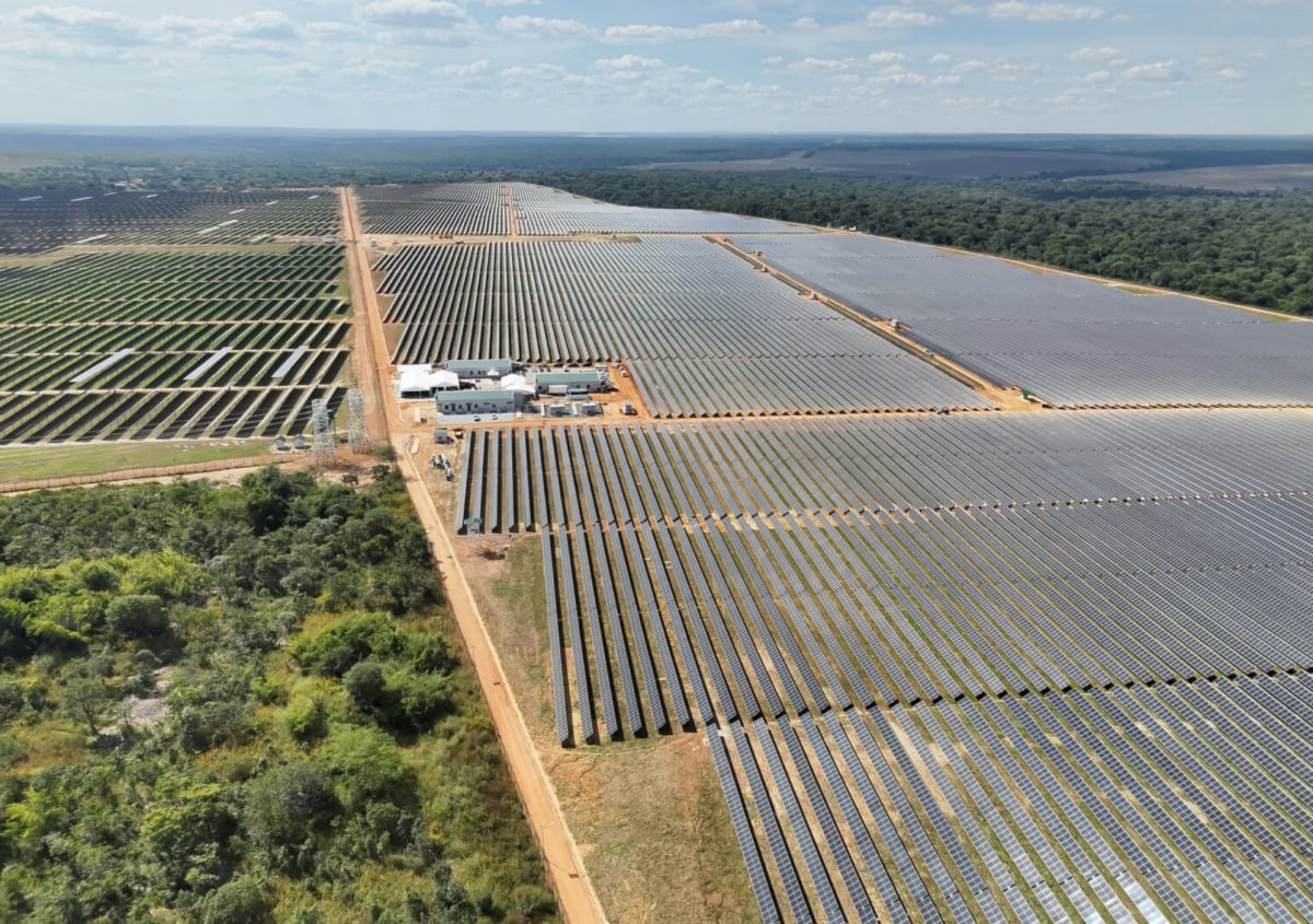 Solar panel arrays stretching across Zambian landscape under bright African sun with mining equipment visible in distance