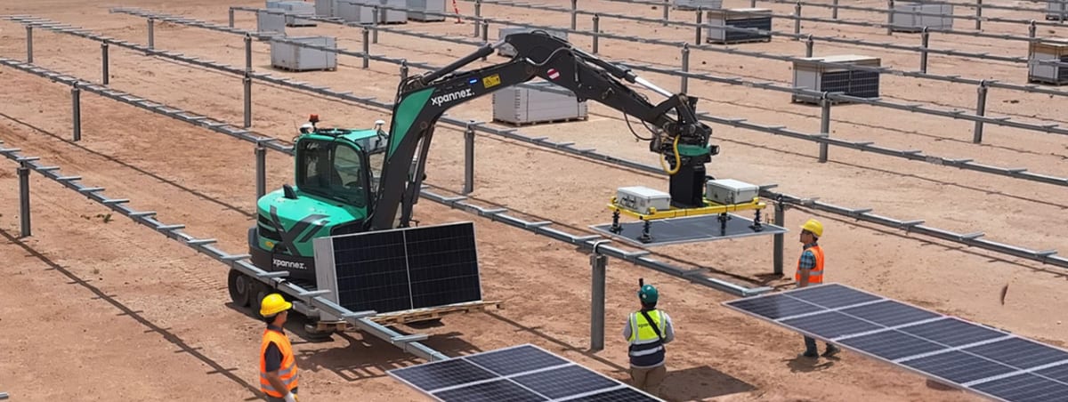 Excavator with robotic arm lifting solar panel at utility-scale solar farm construction site