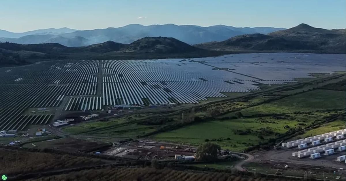 Solar panels stretching across Chilean desert landscape with battery storage facility under bright blue sky
