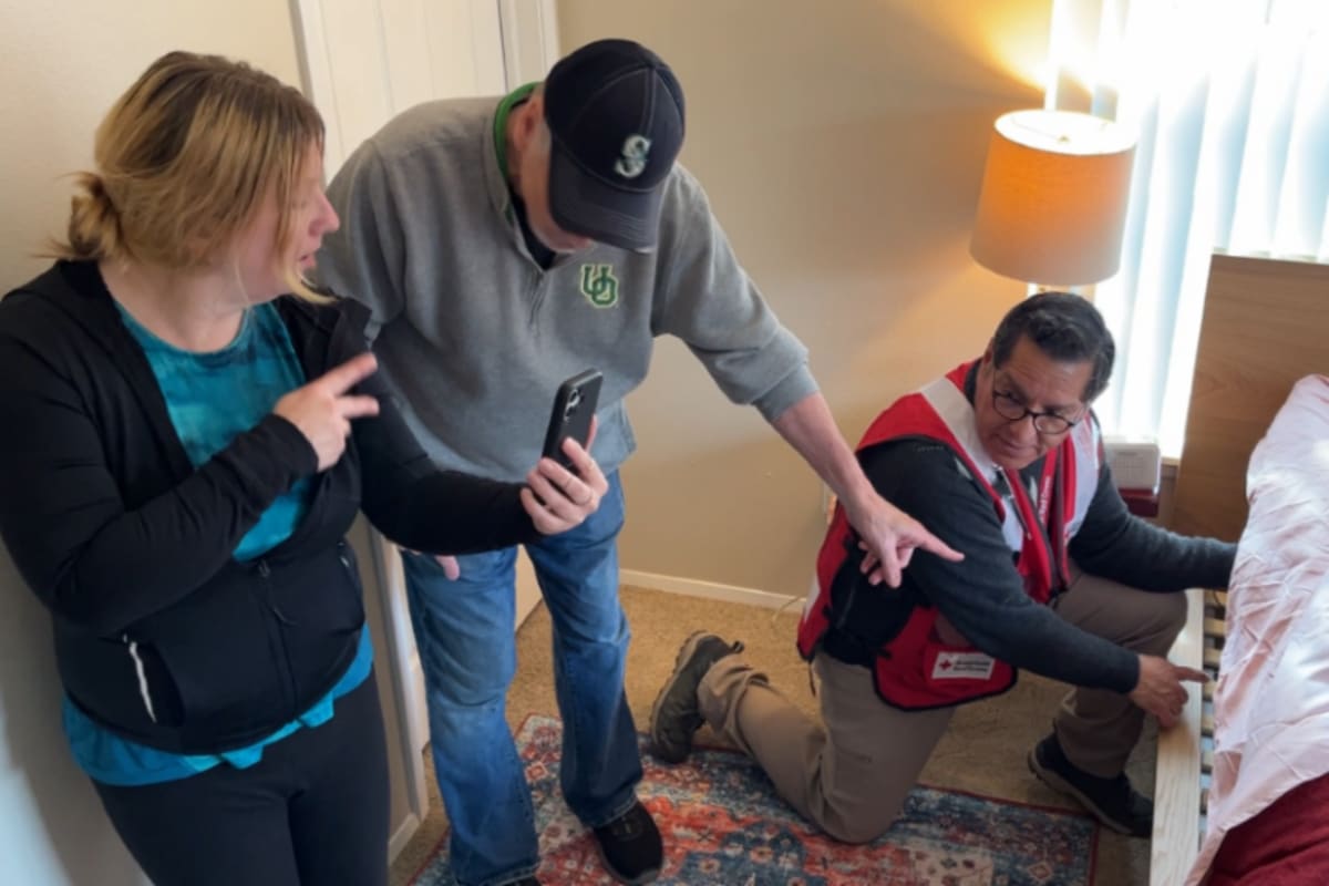 Red Cross volunteer installing bed shaker smoke alarm system under mattress for safety