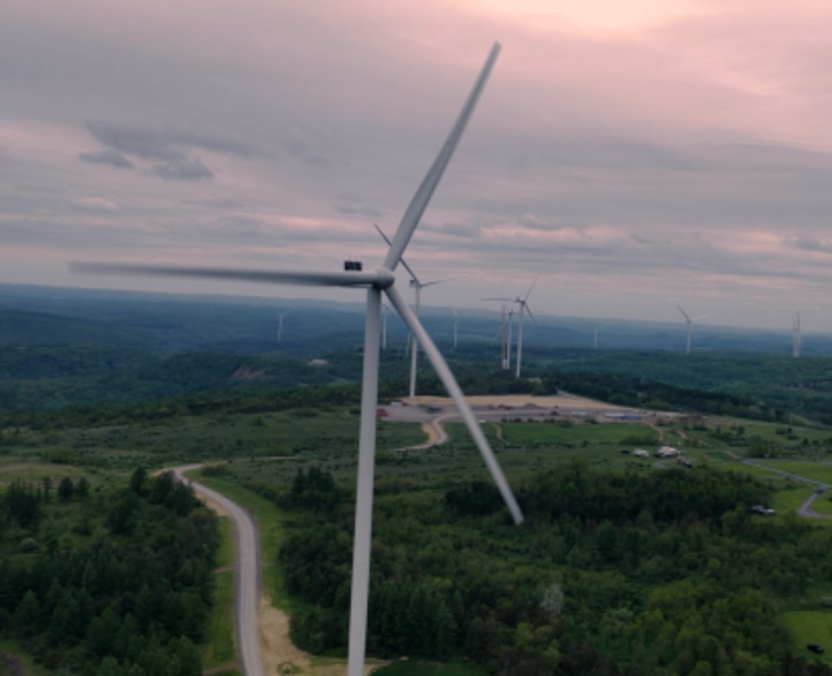 Large white wind turbines standing on rolling Pennsylvania hills with ATV trails visible below