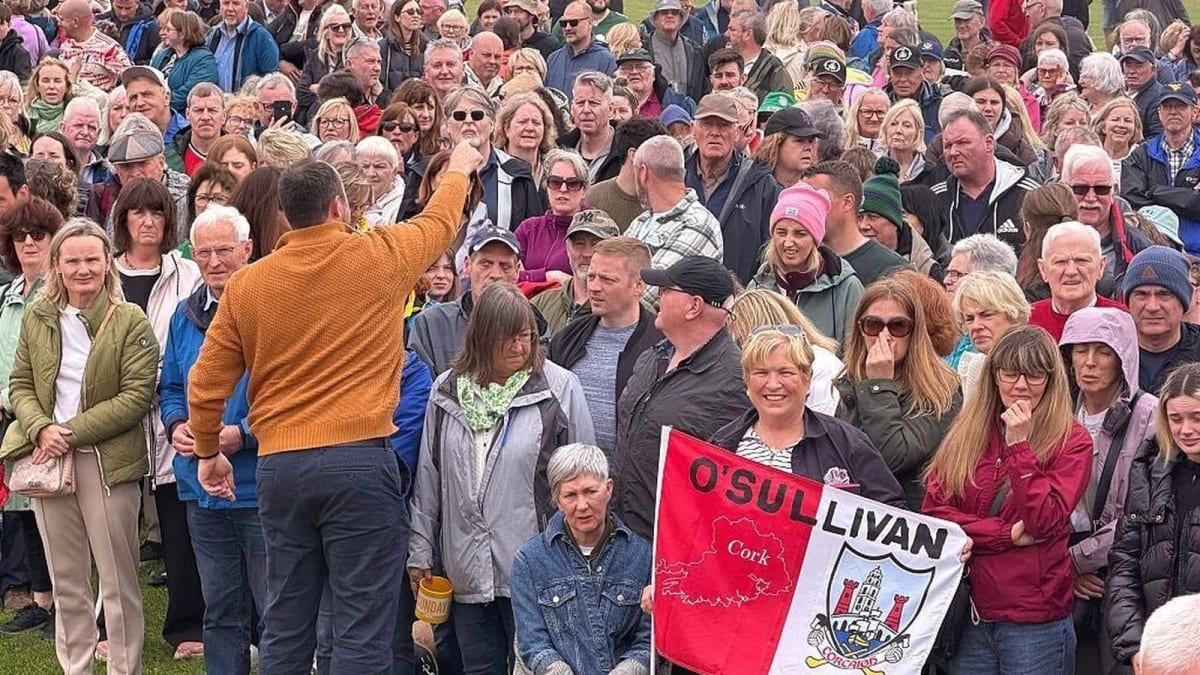 Large crowd of people gathered on school football pitch holding O'Sullivan family crest in Ireland