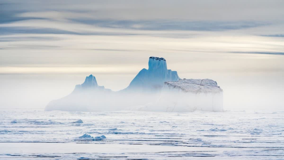 Large white and blue iceberg floating in Arctic waters with brown sediment visible at base