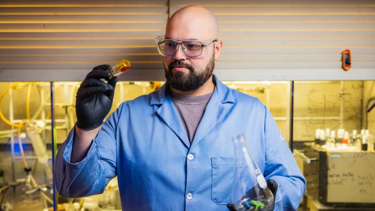 Graduate student holding sample of engine oil created from recycled plastic in chemistry laboratory