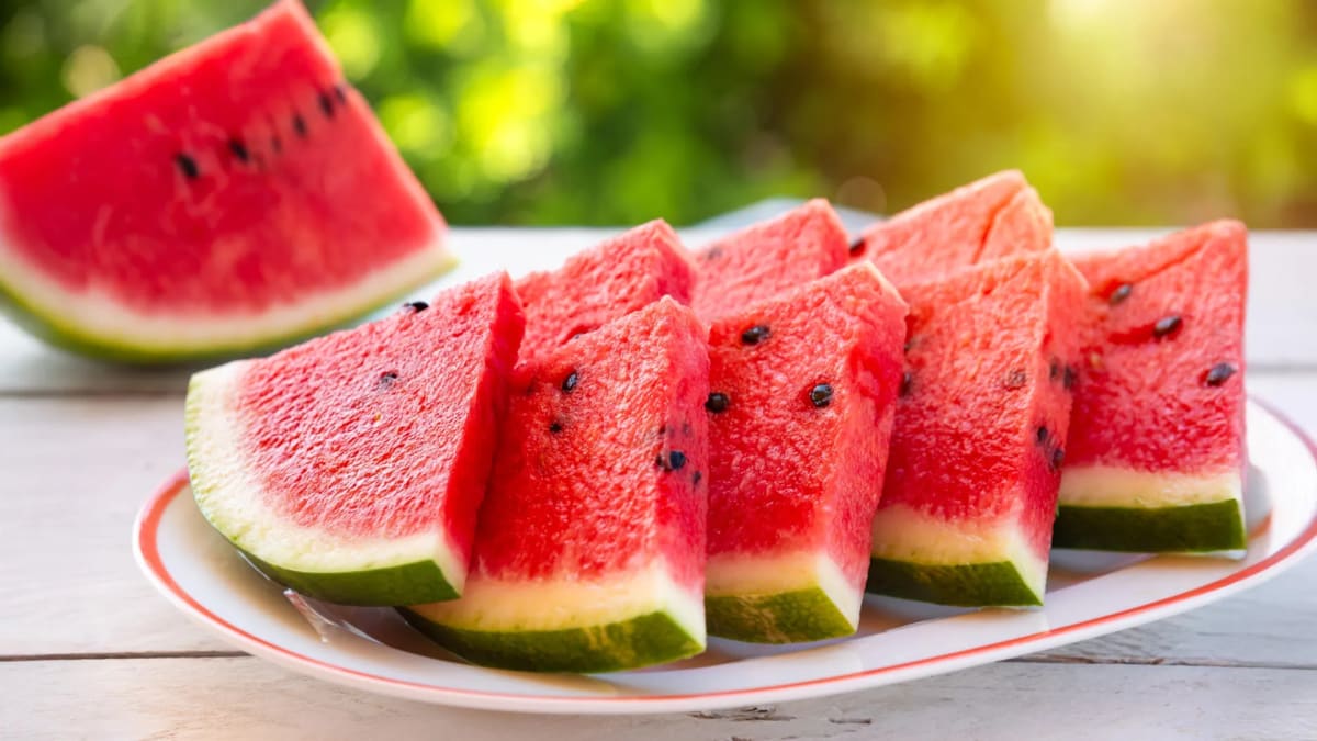 Fresh red watermelon slices arranged on a wooden table in bright summer sunlight