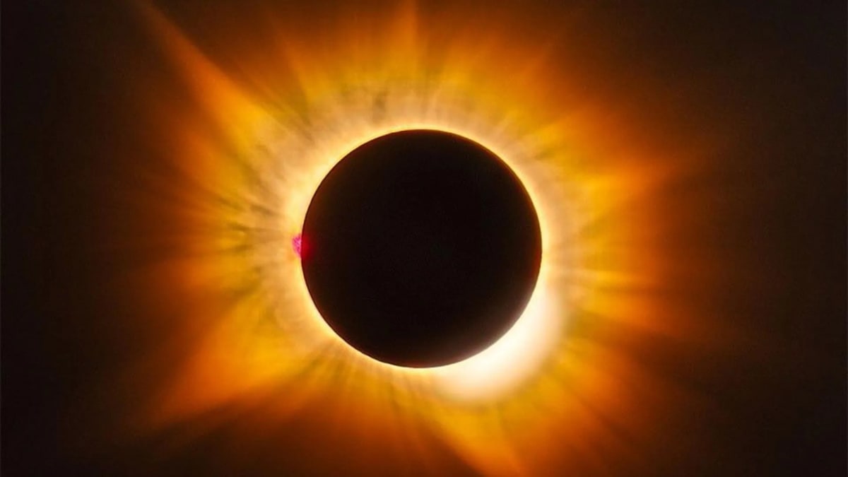 Golden solar eclipse corona with bright pink prominence against darkened sky over Spain