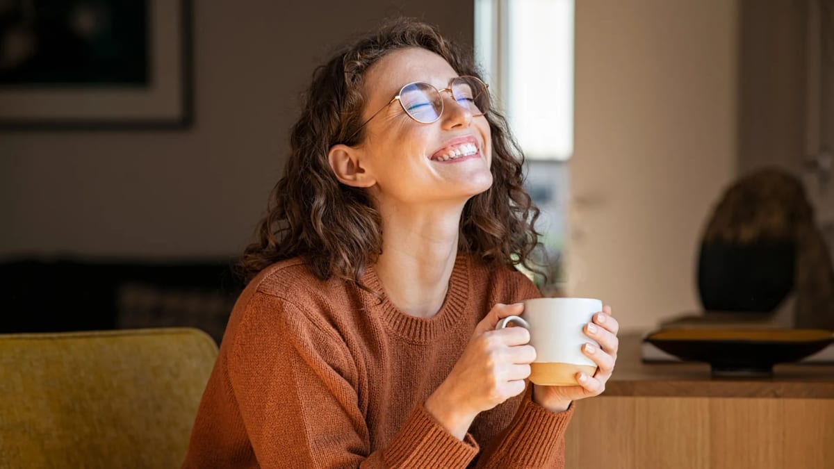 Person holding steaming cup of coffee in morning light with peaceful expression
