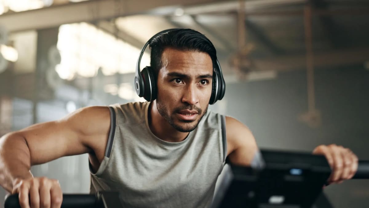 Person wearing headphones and exercising on stationary bicycle in bright gym environment
