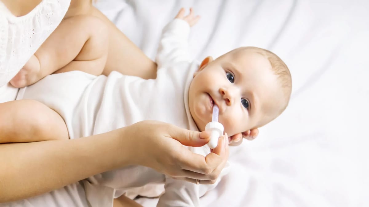 Parent caring for baby with fever, holding infant while checking medicine bottle
