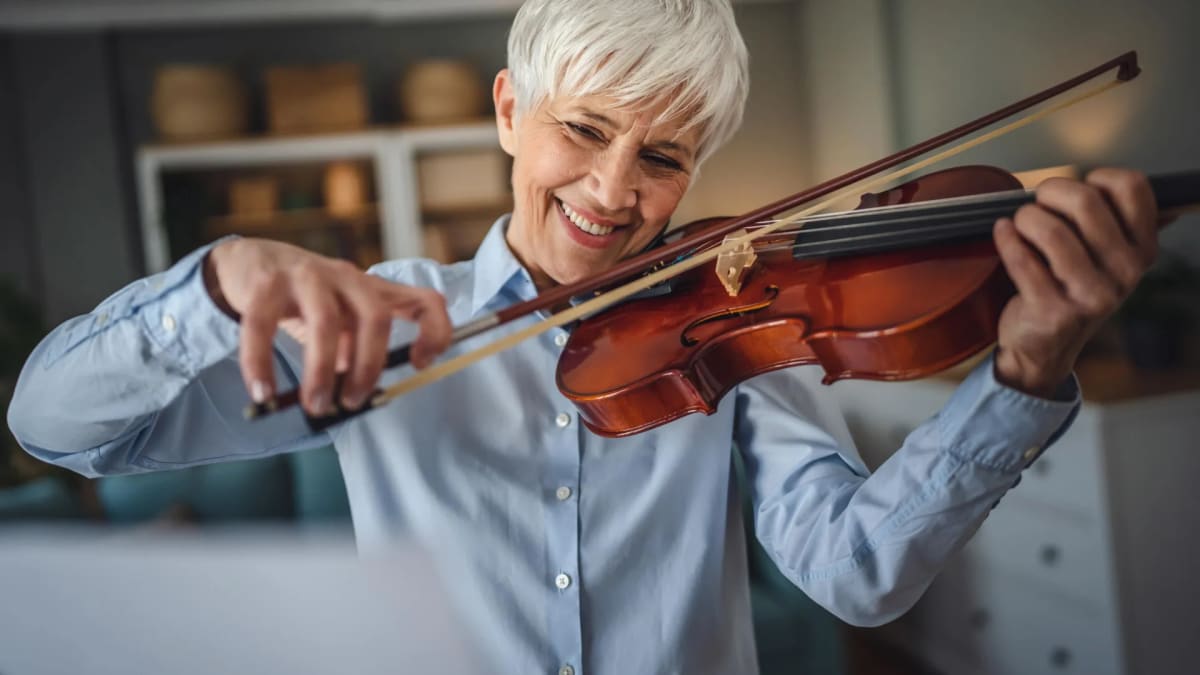 Older adult with gray hair smiling while sitting at piano with sheet music