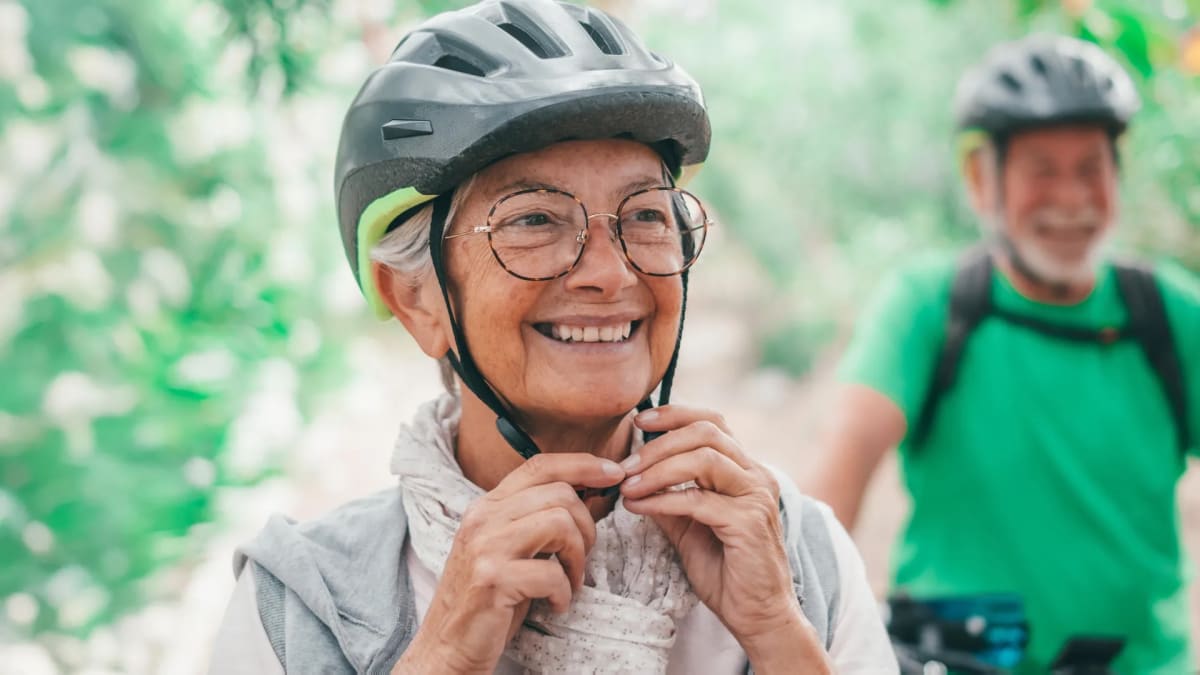 Smiling older adult riding bicycle on sunny path, showing active healthy aging lifestyle