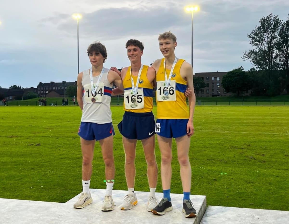 Young male runner crossing finish line on outdoor track during evening competition in Glasgow