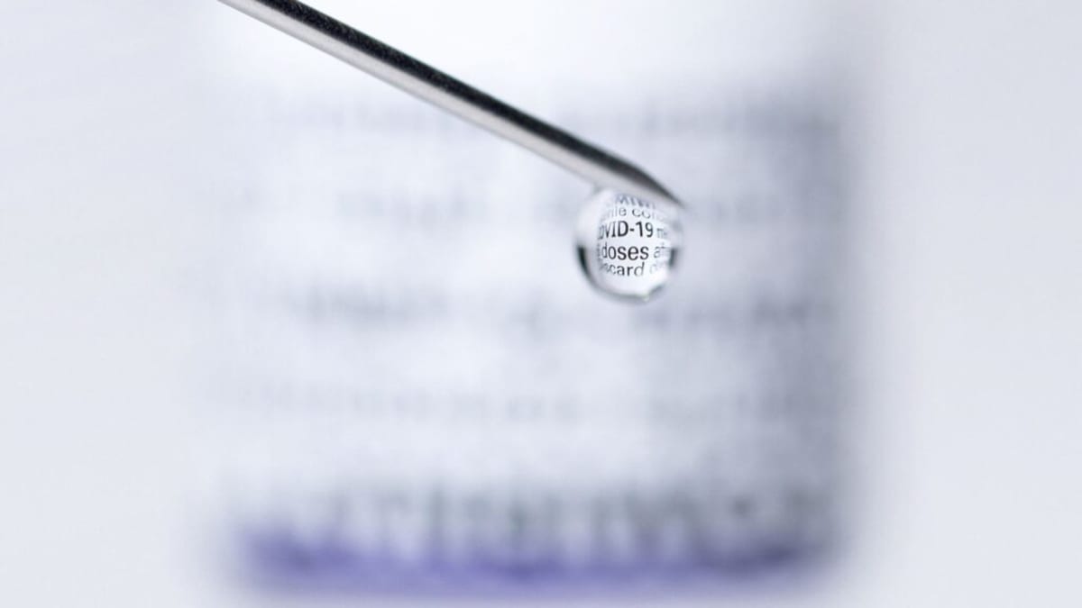 Medical researcher examining vaccine vials in laboratory setting with heart health monitoring equipment visible