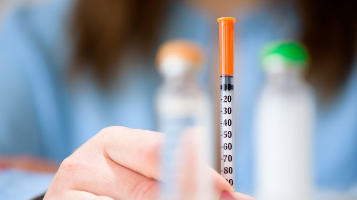 Person holding insulin vial and checking blood sugar monitor at home