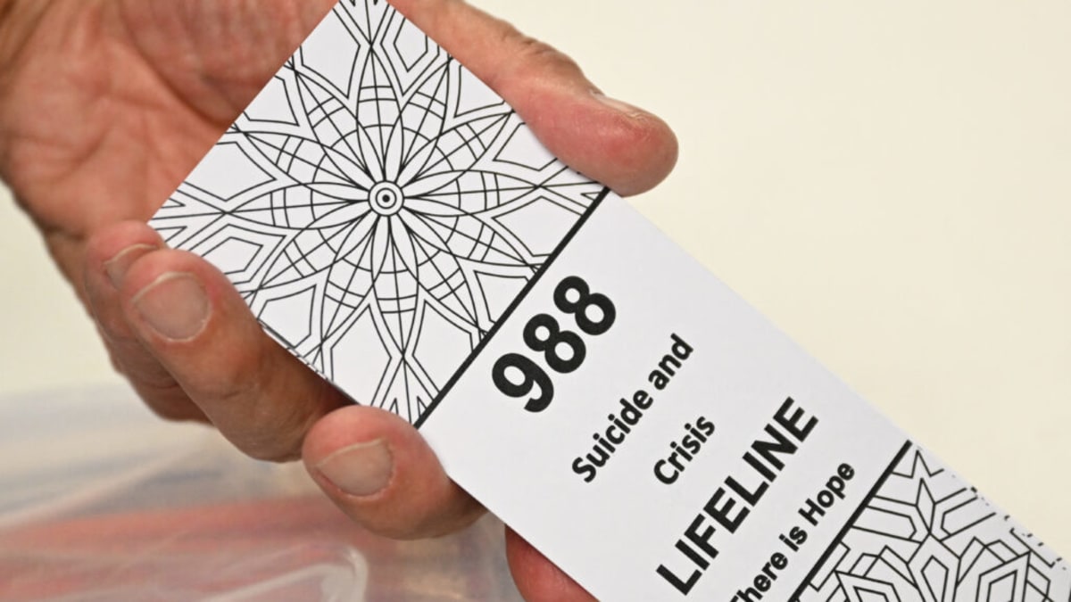Volunteer holds bookmark with Suicide and Crisis Lifeline number for community outreach program