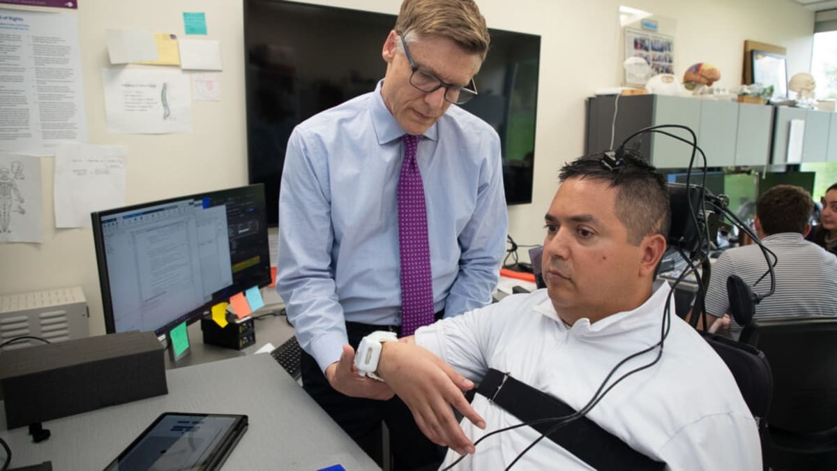 Researcher Chad Bouton helps Keith Thomas with wearable stimulation patch for brain implant study