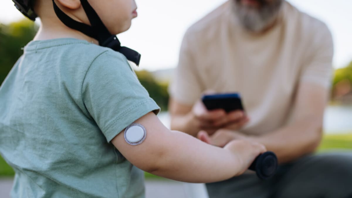 Young child wearing small circular continuous glucose monitor sensor on upper arm