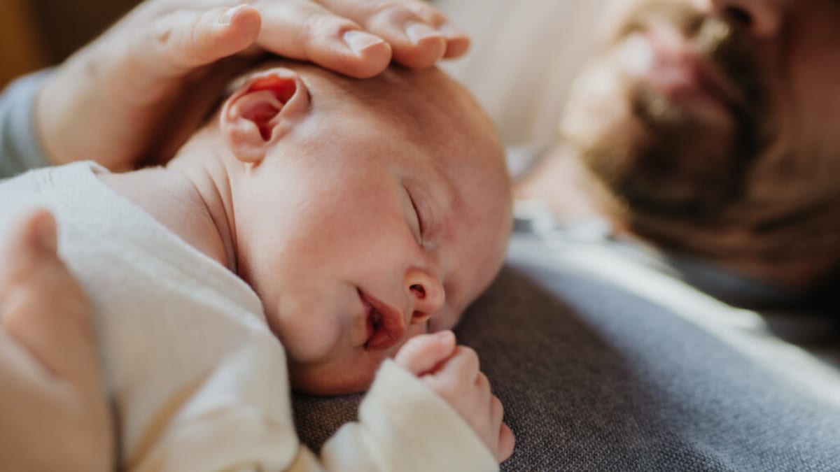 Father holding newborn baby during pediatric checkup in hospital room with doctor present