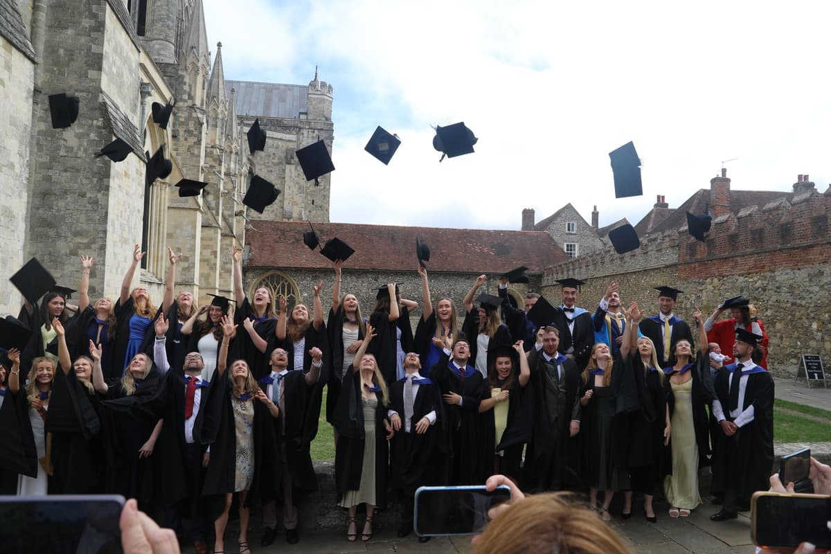 Smiling University of Chichester graduates in caps and gowns celebrate inside historic cathedral