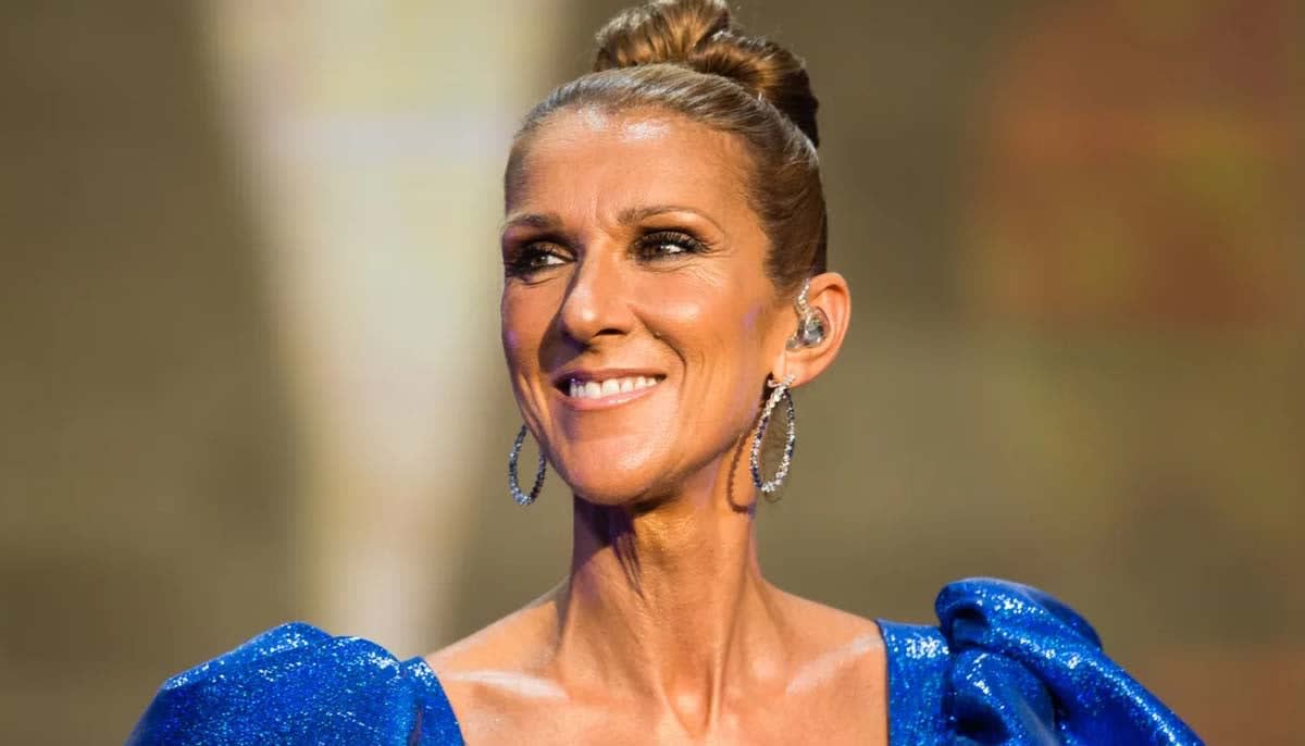 Celine Dion smiling warmly while performing on stage with microphone in hand
