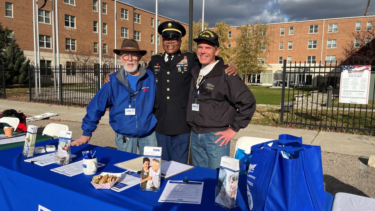 Two veteran volunteers standing with fellow veteran at community event, smiling together