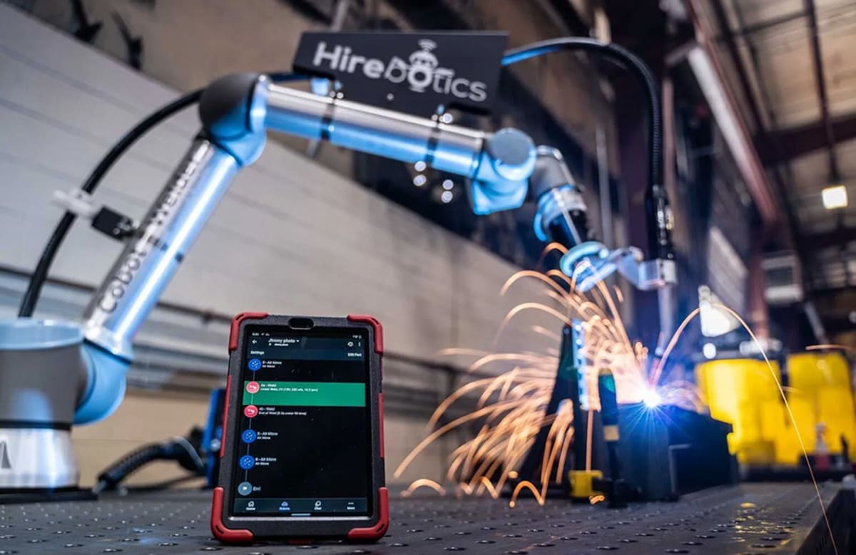 Collaborative welding robot working alongside human welder in metal fabrication shop