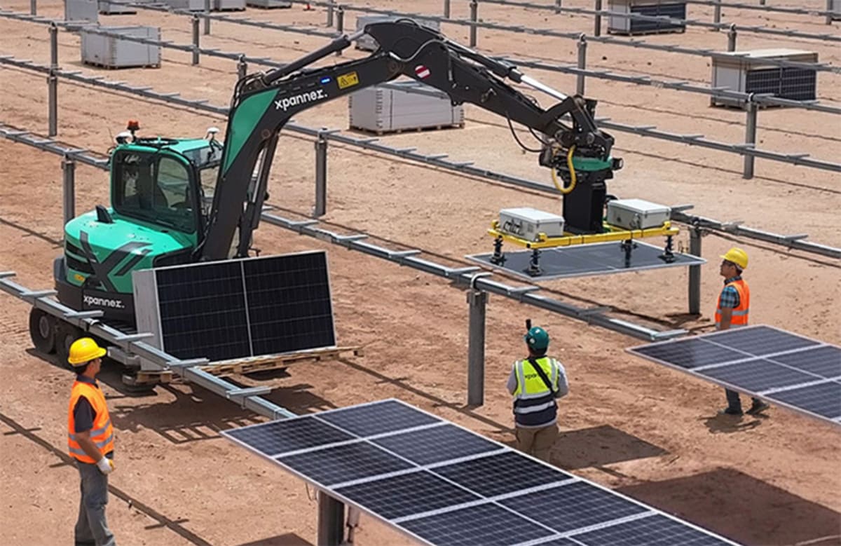 Robotic excavator arm with suction device lifting large solar panel at construction site