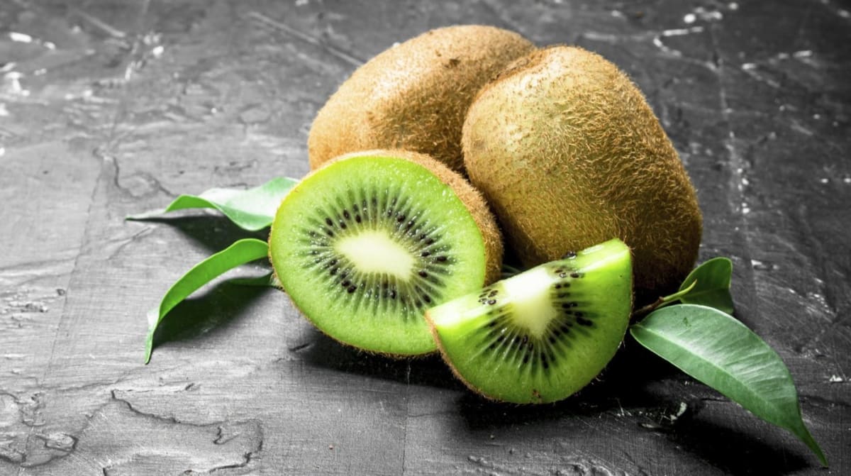 Fresh green and gold kiwifruit cut in half showing vibrant flesh on dark background