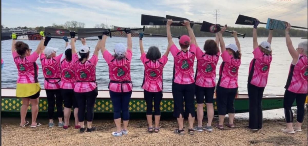 Breast cancer survivors paddling together in synchronized formation on dragon boat at Mercer Lake