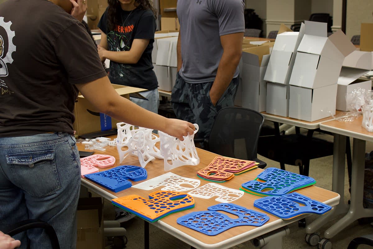 Volunteers organizing dozens of white 3D-printed medical splints and braces on table before shipping to Venezuela