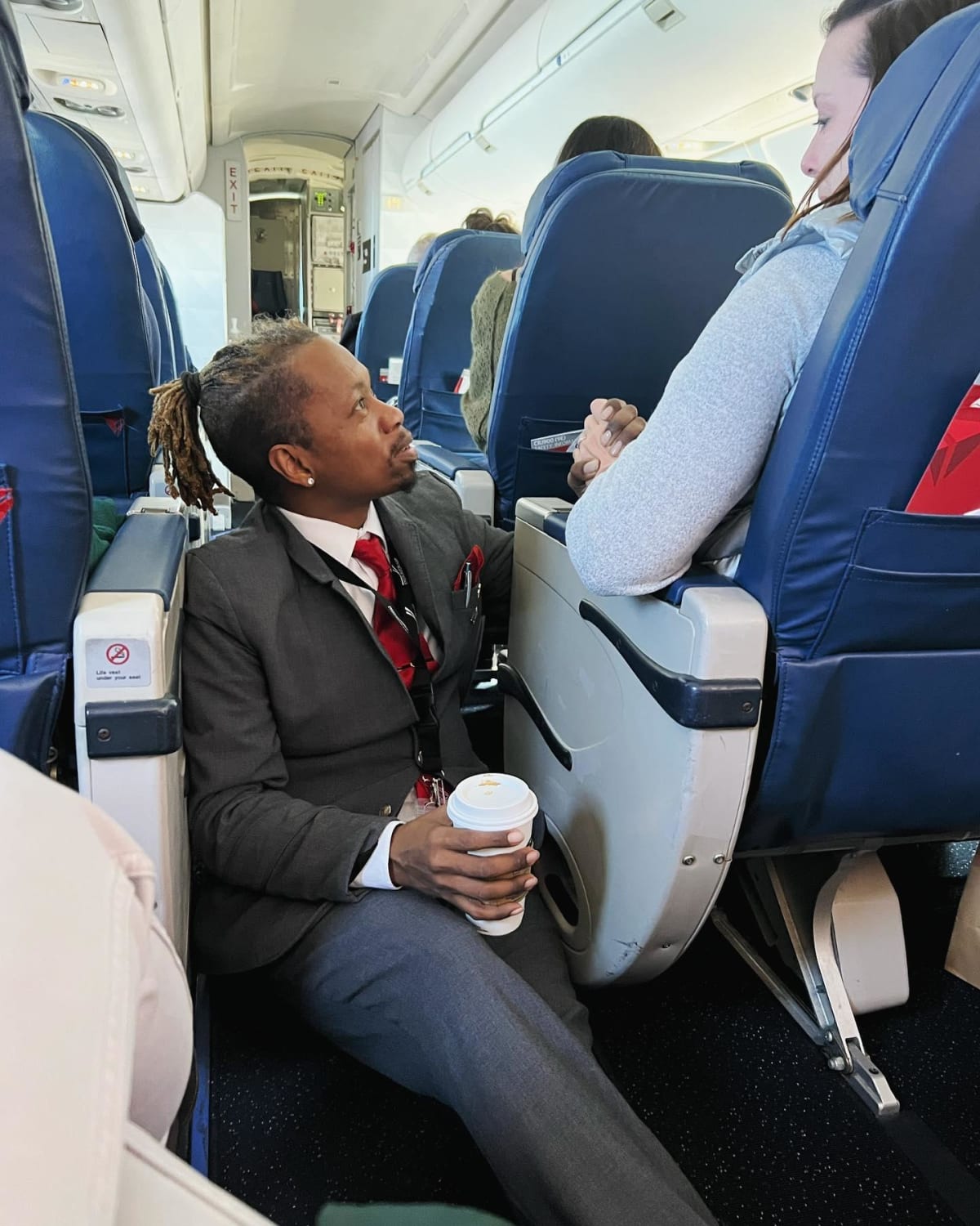 Flight attendant Floyd Dean-Shannon sitting on airplane floor holding nervous passenger's hand