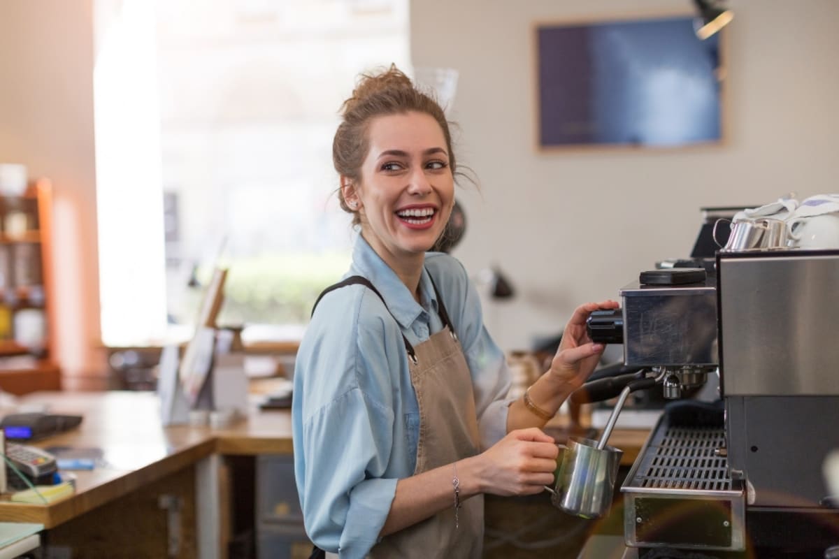 Barista preparing coffee drink behind espresso machine in European cafe setting