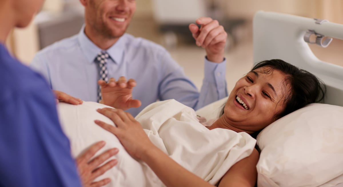 Mom and baby in hospital room with sister holding phone recording the moment