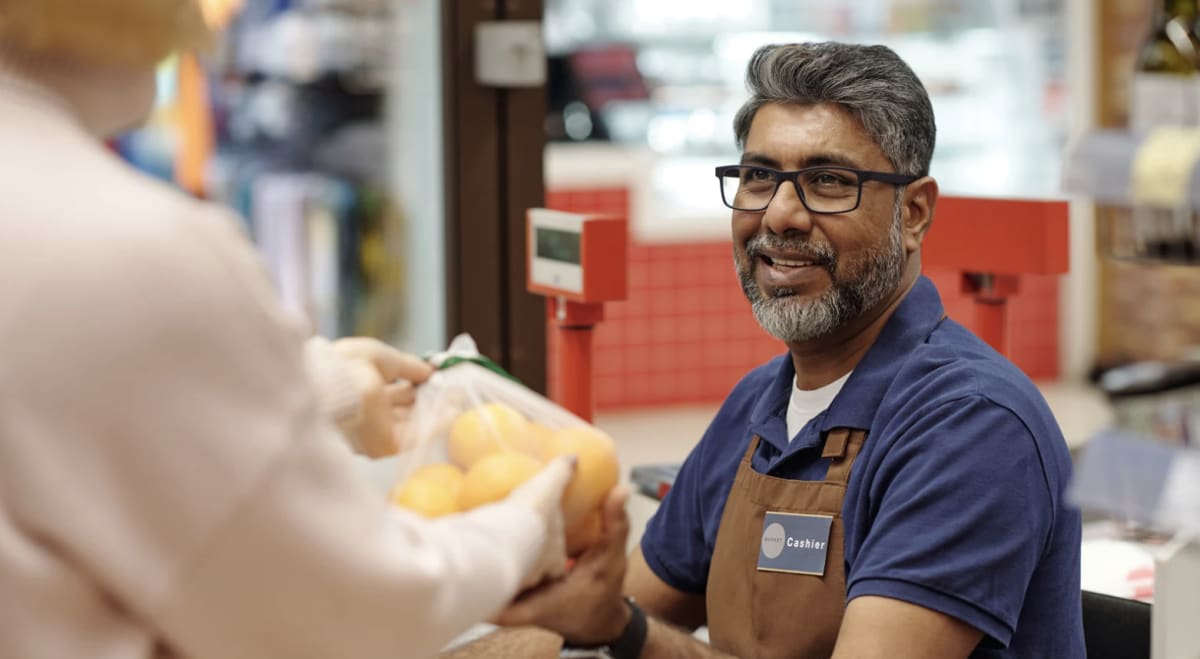 Elderly customer chatting with smiling cashier at checkout lane in Dutch Jumbo supermarket